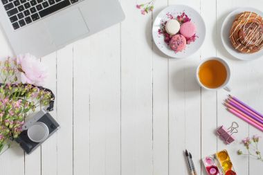 Kadınsı düz çalışma alanı laptop, fincan çay, macarons, fotoğraf makinesi ve beyaz tahta masaya çiçek ile yatıyordu. Üstten Görünüm kadar sahte.