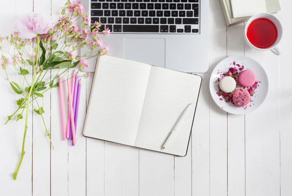 Kadınsı düz çalışma alanı laptop, fincan çay, macarons ve beyaz tahta masaya çiçek ile yatıyordu. Üstten Görünüm kadar sahte.
