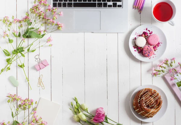 Ženský byt rozložení pracovního prostoru s notebookem, šálek čaje, macarons a květin na bílý dřevěný stůl. Pohled shora mock-up. — Stock fotografie