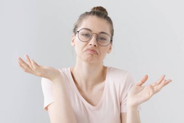 Çaresizlik ve duygusuzluk kol hareketi ile ağız ifade gri arka plan üzerinde izole karışık genç kadın giyiyor trendy hipster gözlük kapalı fotoğrafını belirsiz ifade kavisli.