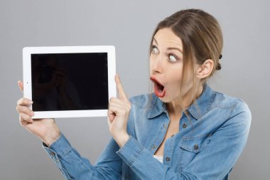 Indoor shot of good-looking woman with makeup isolated on grey background holding blank tablet PC with both hands with emotions of great positive astonishment. Copyspace for commercial offers. clipart