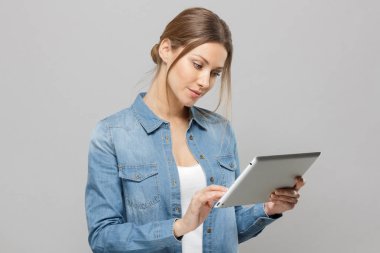 Tablet Pc başını onun elinde ekran Web sayfalarını tarama yaparken dokunmadan ekran doğru hafifçe eğildi tutan çekici doğal güzel Bayan gri arka plan üzerinde izole kapalı resmi.