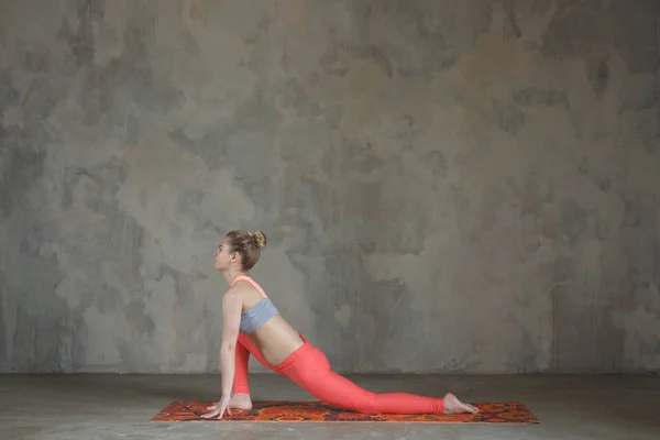 Jovem praticando Ashwa Sanchalanasana, a pose de ioga equestre contra parede texturizada / fundo urbano — Fotografia de Stock