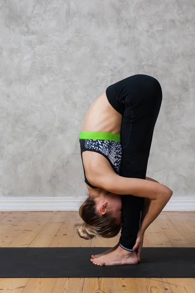 Mujer joven practicando Standing forward bend, Uttanasana yoga pose contra pared texturizada / fondo urbano — Foto de Stock