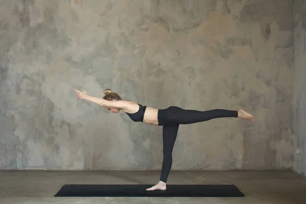 Young woman practicing yoga Warrior pose, Virabhadrasana against texturized wall / urban background — Stock Photo, Image