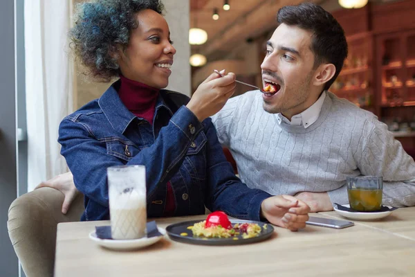 Portrait intérieur de heureux couple mixte déjeuner dans un petit café confortable, afro-américaine fille nourrit son homme bien-aimé dessert mettre cuillère dans sa bouche ouverte, ils ont l'air joyeux et franc . — Photo