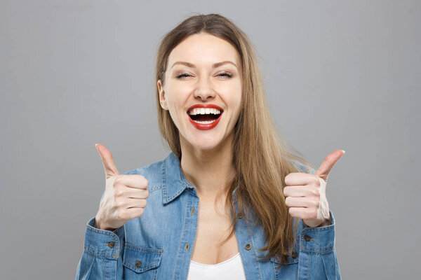 Closeup of young optimistic female isolated on grey background showing thumps up with positive emotions of content and happiness. Copyspace, concept of satisfaction with quality and recommendation.