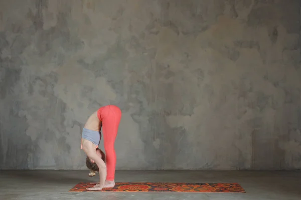Young woman practicing Standing forward bend, Uttanasana yoga po