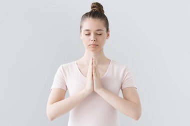 Pembe tişört pratik yoga ve meditasyon, avuç içi bir arada namaste mudra içinde tutan, sakin, rahat ve huzurlu seyir gri arka plan üzerinde izole içinde güzel Avrupa kadın kapalı kapatmak.