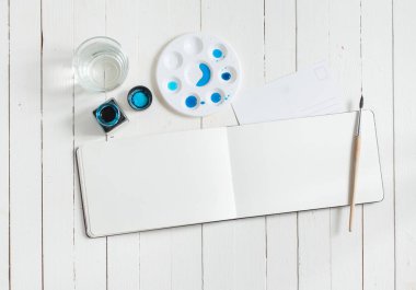 Kadar alay et. Beyaz ahşap masa üzerinde sanatçı çalışma alanı: sketchbook, sulu boya, fırça ve su