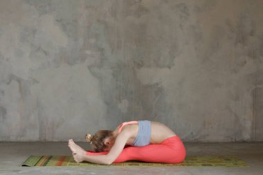 Genç kadın pratik terk etti oturma ileri bend / Paschimottanasana yoga poz tekstüre duvara / kentsel arka plan 