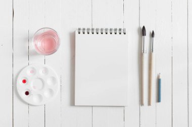 Kadar alay et. Beyaz ahşap masa üzerinde sanatçı çalışma alanı: kırmızı sulu boya, Boya fırçaları ve su