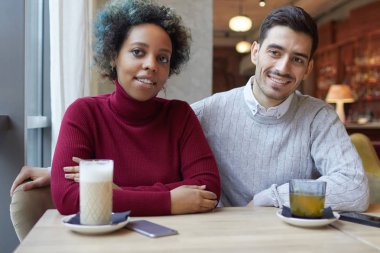 Afro-Amerikan kız ve birlikte bir kafeterya masada öğleden sonra akıllı telefonlar ve içecekler ile masaya oturan beyaz adam kapalı atış, yanındaki bakmak ve küçük gülümseyen şaşkın ve utangaç.