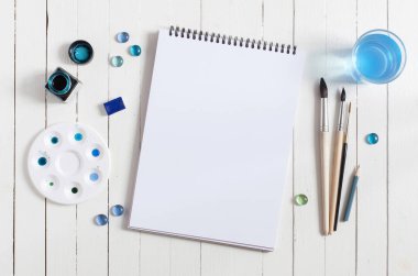 Kadar alay et. Beyaz ahşap masa üzerinde sanatçı çalışma alanı: sketchbook, mavi suluboya, Boya fırçaları ve su