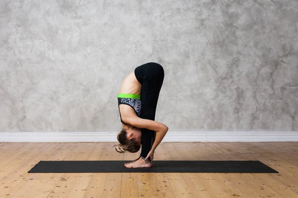 Jovem praticando de pé para a frente curva, Uttanasana ioga pose contra parede texturizada / fundo urbano — Fotografia de Stock