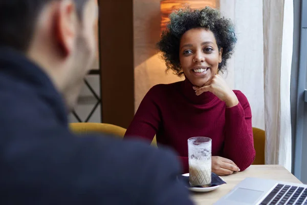 Foto interior de la joven hermosa dama afroamericana sentada en la mesa de la cafetería, sonriendo feliz y mostrando amor, devoción y placer. Raza mixta interracial fecha concepto —  Fotos de Stock