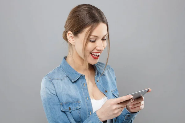 Foto interior de uma mulher bonita vestindo roupas casuais isoladas em fundo cinza olhando agitado na exibição de seu smartphone sorrindo e rindo alegremente, impressionado com o conteúdo de mídia da web . — Fotografia de Stock