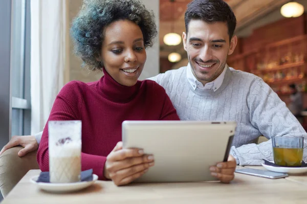 室内拍摄的快乐混合夫妇在共享媒体内容与对方、 利益和幸福的微笑望着平板电脑显示的小咖啡屋享受他们的约会. — 图库照片