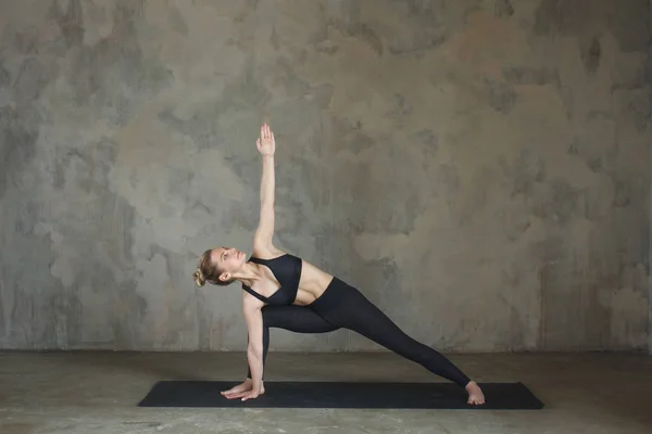 Young woman practicing yoga pose Bikram triangle, Trikonasana against texturized wall / urban background — Stock Photo, Image