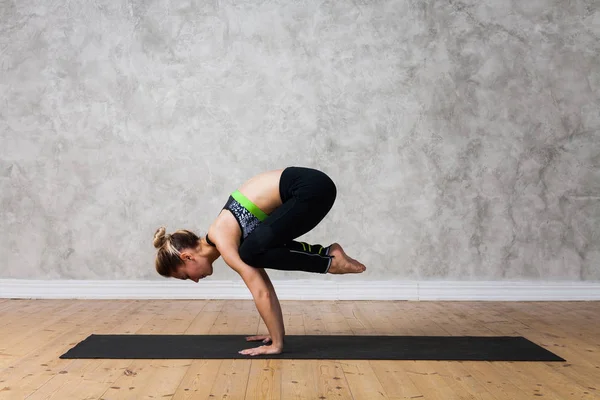 Mujer joven practicando yoga pose grúa, Bakasana contra pared texturizada / fondo urbano — Foto de Stock