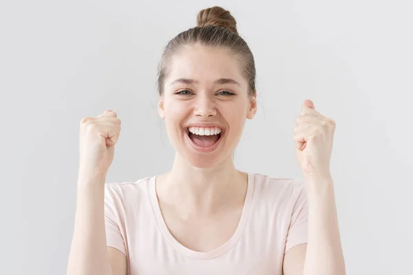 Close-up tiro de jovem mulher positiva isolado em fundo cinza compartilhando seu triunfo, levantando os braços com os punhos, a boca aberta enquanto ela está sorrindo e rindo feliz e emocionalmente . — Fotografia de Stock
