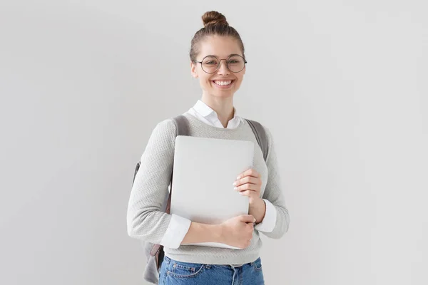 Retrato de jovem europeia de pé isolado em fundo cinza, segurando laptop fechado com sorriso amigável positivo, ansioso para estudar, aprender e fazer progressos na carreira . — Fotografia de Stock