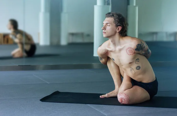 Handsome tattooed man practicing yoga. Young male teacher medit