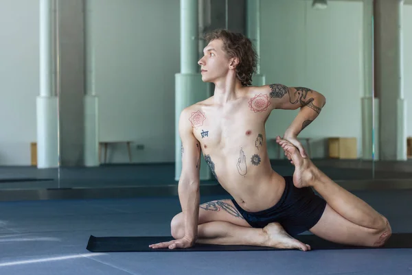 Handsome tattooed man practicing yoga. Young male teacher takin