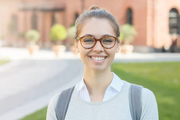 Retrato de close-up de boa aparência menina estudante universitário feliz, vestindo grandes óculos de moda e mochila cinza, seu cabelo amarrado em coque, sorrindo amigável para a câmera, sentindo-se satisfeito e alegre . — Fotografia de Stock