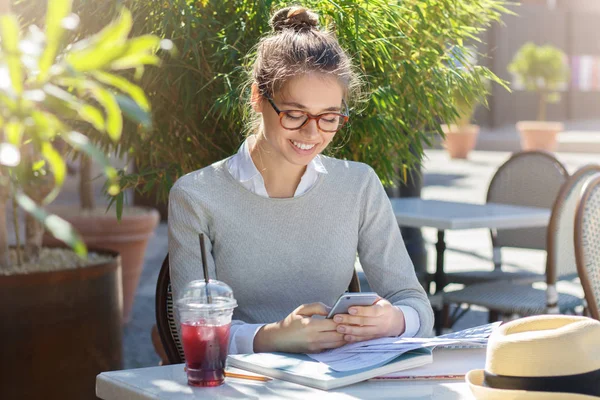 Yatay güneşli yaz öğleden sonra zevk mutlu güzel kız portresi o suyu içme ve dokunmatik cep telefonu iletişim ile arkadaş kalmak açık sokak Cafe harcamaktadır