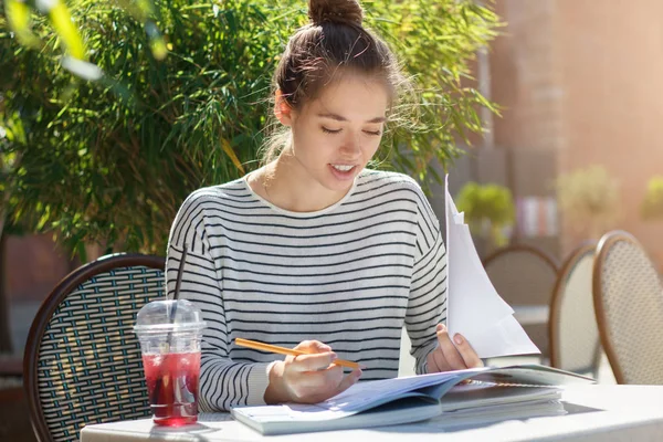 Closeup picture of young beautiful European woman dressed casually without makeup sitting at table in outdoor cafe, checking data in papers and correcting, looking responsible and concentrated — Stock Photo, Image