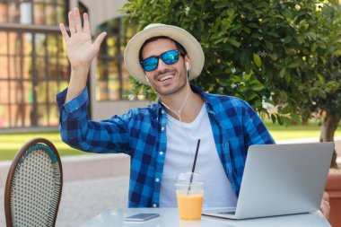 Yatay resim genç gülümseyen Avrupa açık Cafe dışarı yemek yerken dizüstü bilgisayarda çalışma masasında harcama zaman adamım, açık elle onun arkadaşı tebrik jest iletişim kurmak için istekli