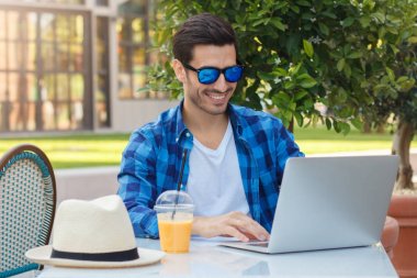 Portre resim trendy esunglasses giyen genç Avrupa iş adamı, kulaklık ile dizüstü bilgisayarda çalışırken ekran dikkatle isteyen iş online için geçerli projeleri ile ilgili