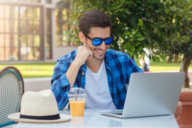 Yatay rahat kıyafetler boş zamanlarınızı çalışma veya dizüstü bilgisayarda iletişim, mutlu bir şekilde ekrana bakarak ve gülümseyen harcama açık sokak Cafe masada oturan genç olumlu adam portresi