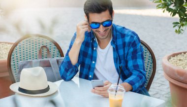 Sevgili ve en yakın Telefona kulaklık olumlu içerik paylaşımı ile iletişim sırasında açık kafe öğleden sonra harcama rahat kıyafetler içinde Avrupa yakışıklı yatay yaz fotoğrafı