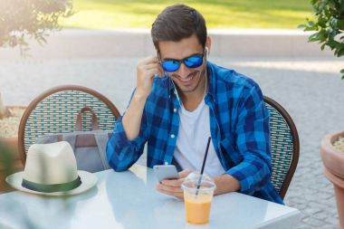 Genç beyaz erkek boş zamanlarında açık kafe, taze portakal suyu içme geçiriyor gibi dinlerken dostum ya da ses içeriği Web için cep telefonunu görüntüsünü görüntülemenin Closeup fotoğraf