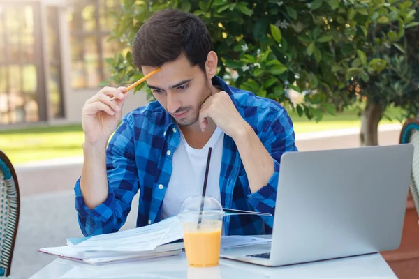 Imagen de primer plano del joven empresario ocupado que trabaja con papeles mientras está sentado en la mesa de la cafetería al aire libre, mirando muy serio y atento concentrado para no cometer ningún error al comprobar —  Fotos de Stock