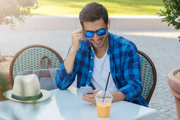 Genç beyaz erkek boş zamanlarında açık kafe, taze portakal suyu içme geçiriyor gibi dinlerken dostum ya da ses içeriği Web için cep telefonunu görüntüsünü görüntülemenin Closeup fotoğraf