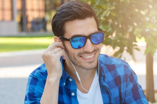 Genç iyimser Avrupa erkek harcama zaman dışında iyi haber paylaşımı arkadaşı ile onun smartphone, kulaklık arıyorum memnun kullanarak ve olumlu gülümseyen kafeterya masada closeup headshot