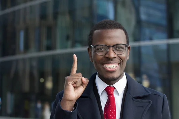 I have an idea! Handsome african american businessman in glasses keeping finger pointed upwards, showing something above his head, making gesture with index finger. Eureka, solution sign concept