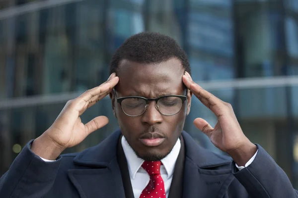 Retrato urbano de cara de pele escura estressado vestindo roupas formais tocando templos com os dedos, olhos fechados, sentindo-se responsável por encontrar solução para o problema crucial conectado com seu negócio — Fotografia de Stock