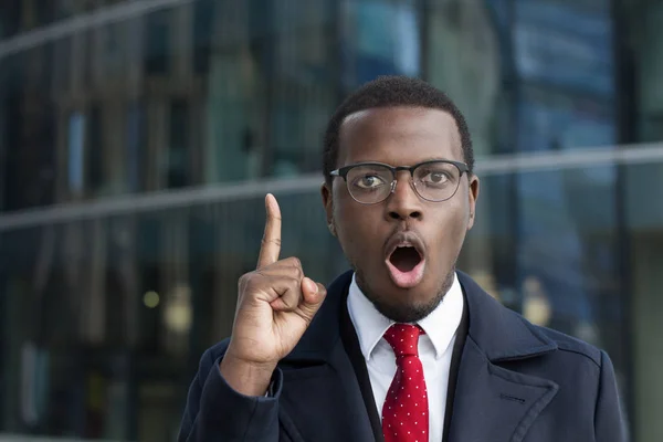 Retrato urbano de empresário afro-americano emocional retratado no centro da cidade olhando para a câmera com olhos redondos e boca aberta com dedo indicador levantado como se tivesse encontrado solução para o problema — Fotografia de Stock