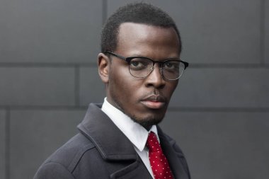 Afrika kökenli Amerikalı girişimci koyu gri duvara izole ayakta yatay headshot giymiş siyah ceket, beyaz gömlek ve kırmızı kravat, konsantre ve ciddi, düşünme planları hakkında arıyorum