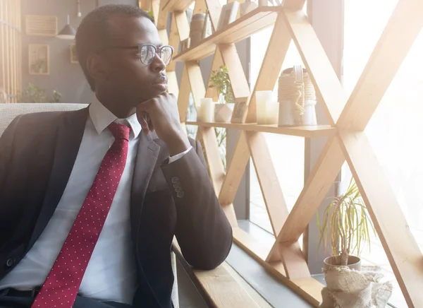 Yatay closeup yakışıklı Afrikalı-Amerikalı iş adamı boş zamanlarında kapalı kahvehane sokağa düşünce ve kaygıları dolu şık gözlük seyir harcama