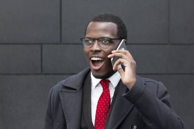 Sokakta şehir merkezinde genç Afrika erkek ayakta açık portre resmi takım elbise, beyaz gömlek ve kravat, sokak izlerken, neşeli bir gülümseme ile telefonda konuşurken, iş konuları tartışırken giyinmiş