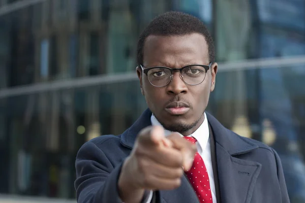 Horizontal headshot of alert african executive standing outdoors in business part of city drawing attention to user with forefinger as if emphasizing something important