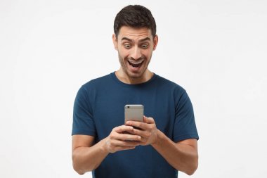 Çekim portre genç adamın gri arka plan üzerinde izole kapatmak, seyir gülümsediğini smartphone görüntüleme heyecanlı ve gülerek mutlu bir şekilde, medya içeriği web üzerinden hayran bırakmak yanında