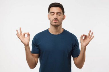 Concentrated relaxed man in blue t-shirt with closed eyes, having relaxation while meditating, trying to find balance and harmony. Yoga and meditation concept