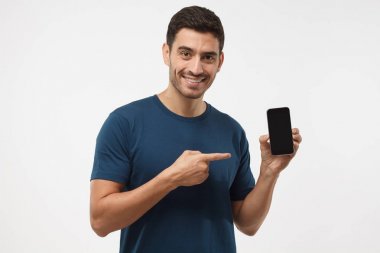 Atış hansome adamın t-shirt üzerinde izole mavi akıllı telefon sunulması ve boş siyah perde ile boşaltmak reklamlar için parmağınızla işaret eden arka plan, gri