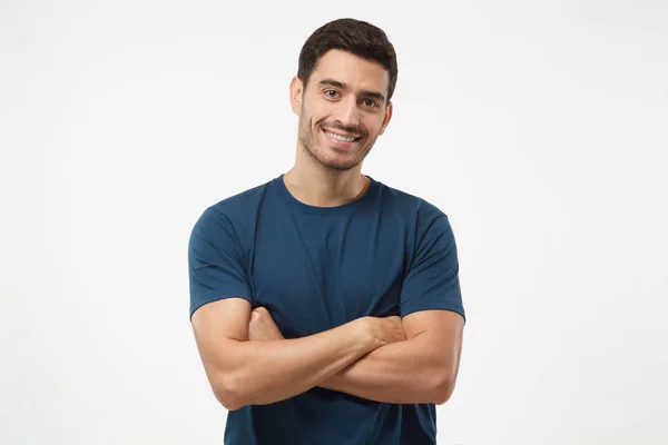 Portrét usměvavý pohledný chlap v modré tričko stojící s překřížením rukou izolované na šedém pozadí — Stock fotografie